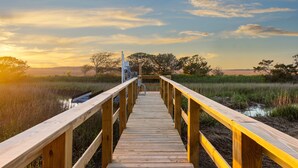 Un muelle de madera que lleva a una estructura con barandilla metálica, rodeada de paisaje natural y árboles.