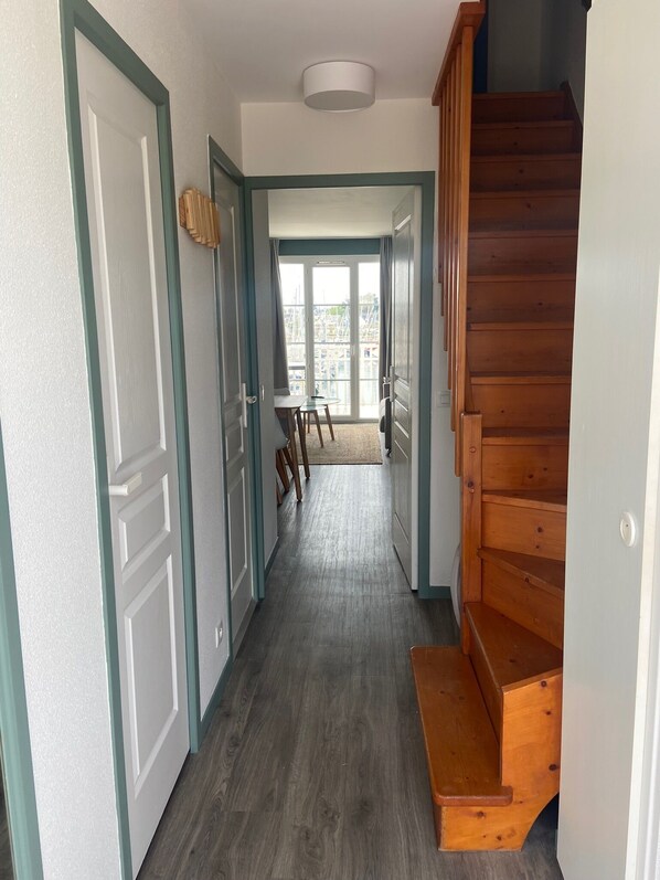 A hallway with a wooden staircase, a view of the outside through a glass door, and a small table with chairs.