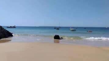 Una playa con cielos despejados, aguas tranquilas y barcos.