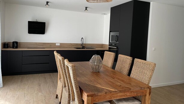 A modern kitchen with a wooden dining table and wicker chairs, a black cabinet, and a flat-screen TV mounted on the wall. - Villa 3 bedrooms 900 m from Lac de Parentis (Parentis-en-Born)