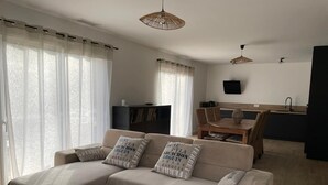 A modern living room with a sofa, a coffee table, and a dining area with a table and chairs. - Villa 3 bedrooms 900 m from Lac de Parentis (Parentis-en-Born)