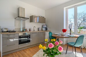 Una cocina moderna con horno empotrado, microondas y lavaplatos. Cuenta con un comedor con mesa y sillas, y vistas al exterior a través de un ventanal grande.