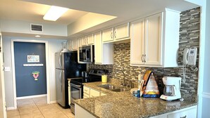 A modern kitchen with white cabinets, granite countertops, stainless steel appliances, and a tiled backsplash. - Surf Side Shores 1906 | 3 bd 3 ba | gulf-front  (Gulf Shores)