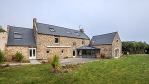 A stone house with a sloped roof, a covered porch, and a grassy yard. - LA LONGERE DU TERTRE - Charmante longère proche plage (Cancale)