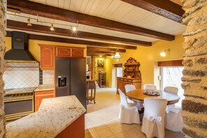 Une cuisine avec des poutres en bois, un mur en pierre et un coin repas comprenant des chaises et une table.