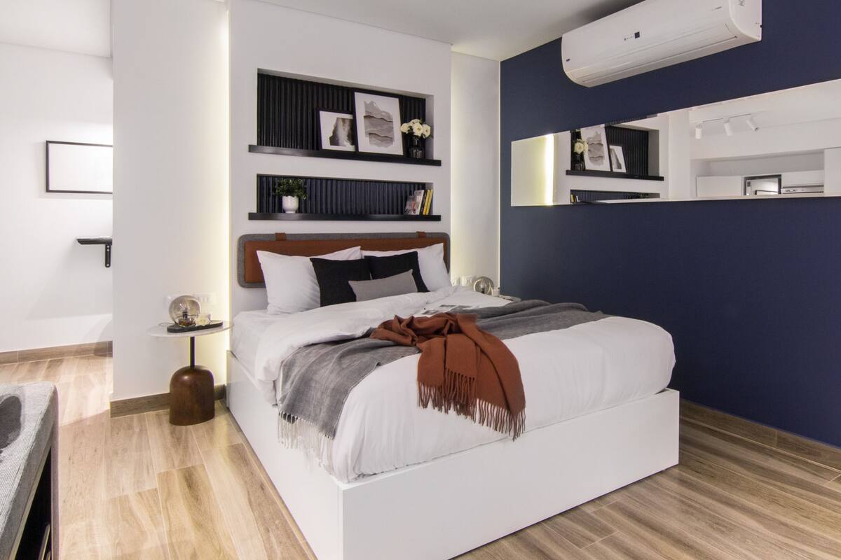 Un dormitorio moderno con una cama grande, una mesita de noche, un armario auxiliar, aire acondicionado empotrado y un estante con adornos.