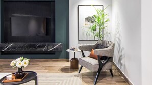 A modern living room with a flat-screen TV, a comfortable armchair, a small table with a vase of flowers, and a decorative plant.
