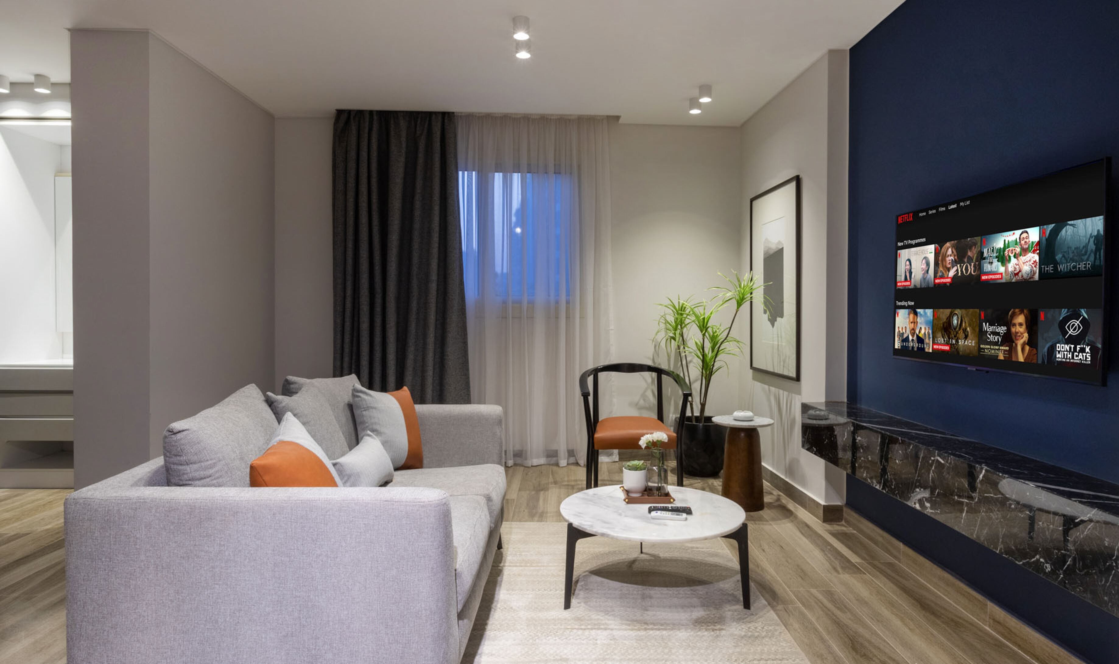 Uma sala de estar moderna com um sofá cinza, uma mesa de centro e uma TV na parede exibindo a interface da Netflix.