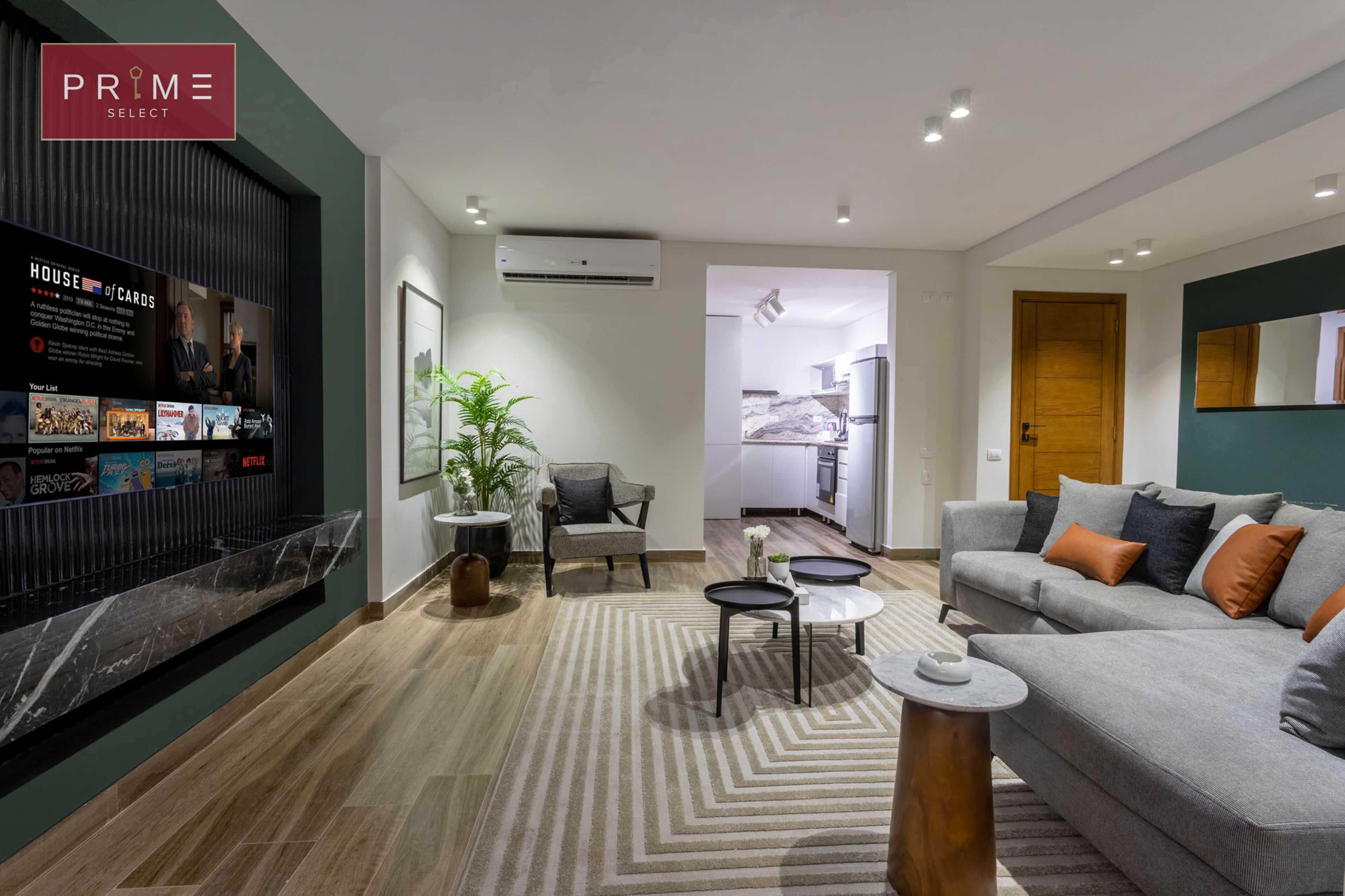 A modern living room with a sofa, armchairs, a coffee table, and a TV displaying 'House of Cards'.