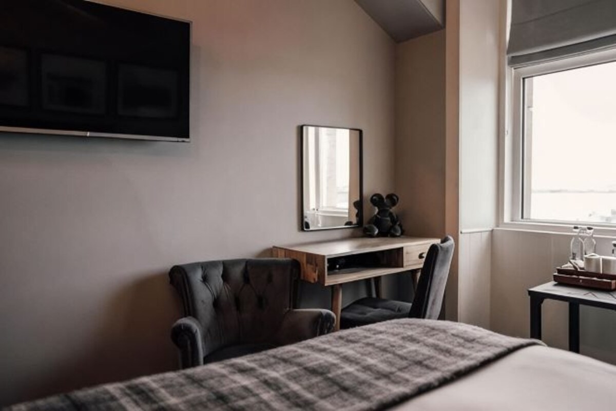 A hotel room with a bed, a desk with a chair, a TV mounted on the wall, and a window.