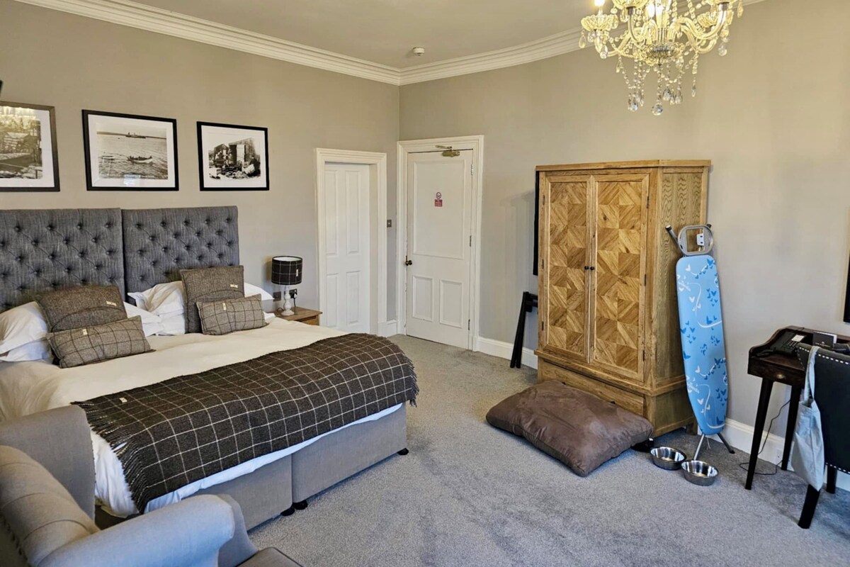 A bedroom with a large bed, a wardrobe, a desk, and a chandelier.
