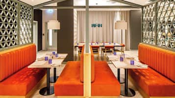 Un restaurante con cabinas y una mesa larga, ambos con cojines anaranjados.