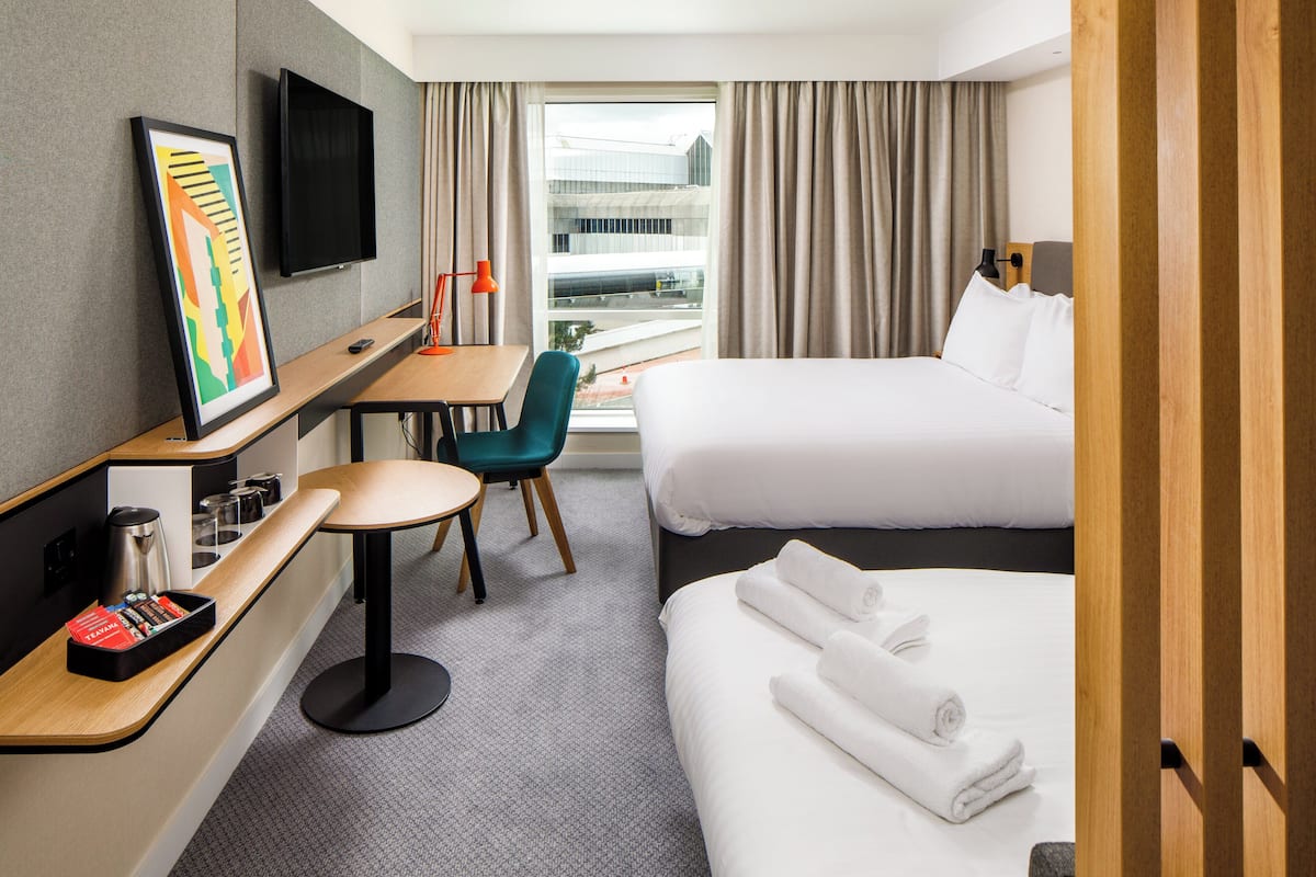 Ein Hotelzimmer mit einem Bett, einem Schreibtisch mit Stuhl, einem an der Wand befestigten Fernseher und einem Fenster mit Vorhängen.