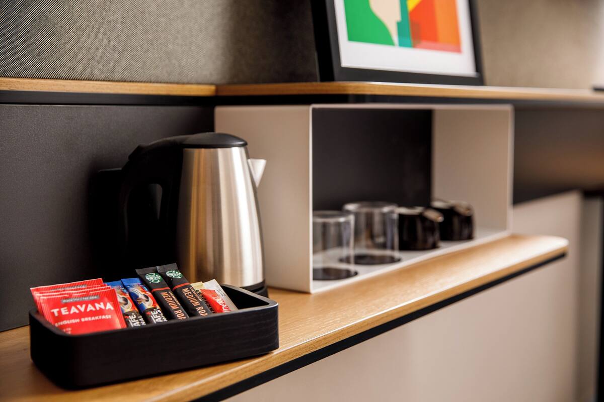 Eine Hotelminibar mit Kaffeemaschine, einem Glasbehälter und einer Packung Teebeuteln.