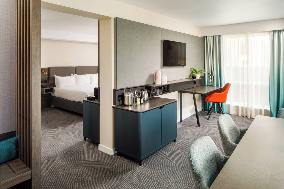 Ein Hotelzimmer mit Bett, Schreibtisch mit Stuhl, Fernseher und einem Fenster mit Vorhängen.