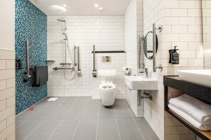 A modern bathroom with a white toilet, a sink, a mirror, and a shower area. - Holiday Inn Manchester Airport by IHG (Manchester)