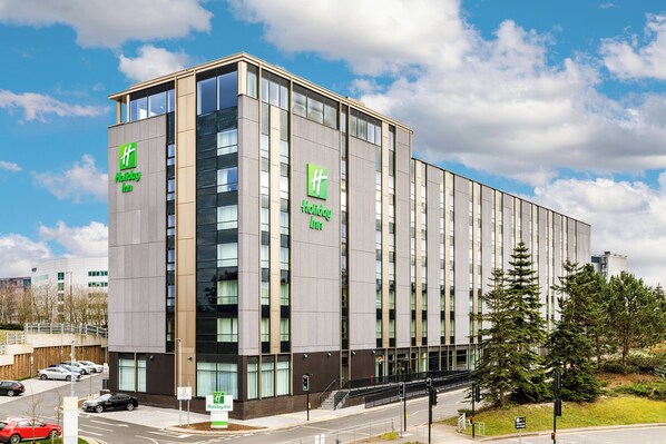 A modern Holiday Inn hotel with a prominent facade, large windows, and a parking area visible in the foreground. - Holiday Inn Manchester Airport by IHG (Manchester)