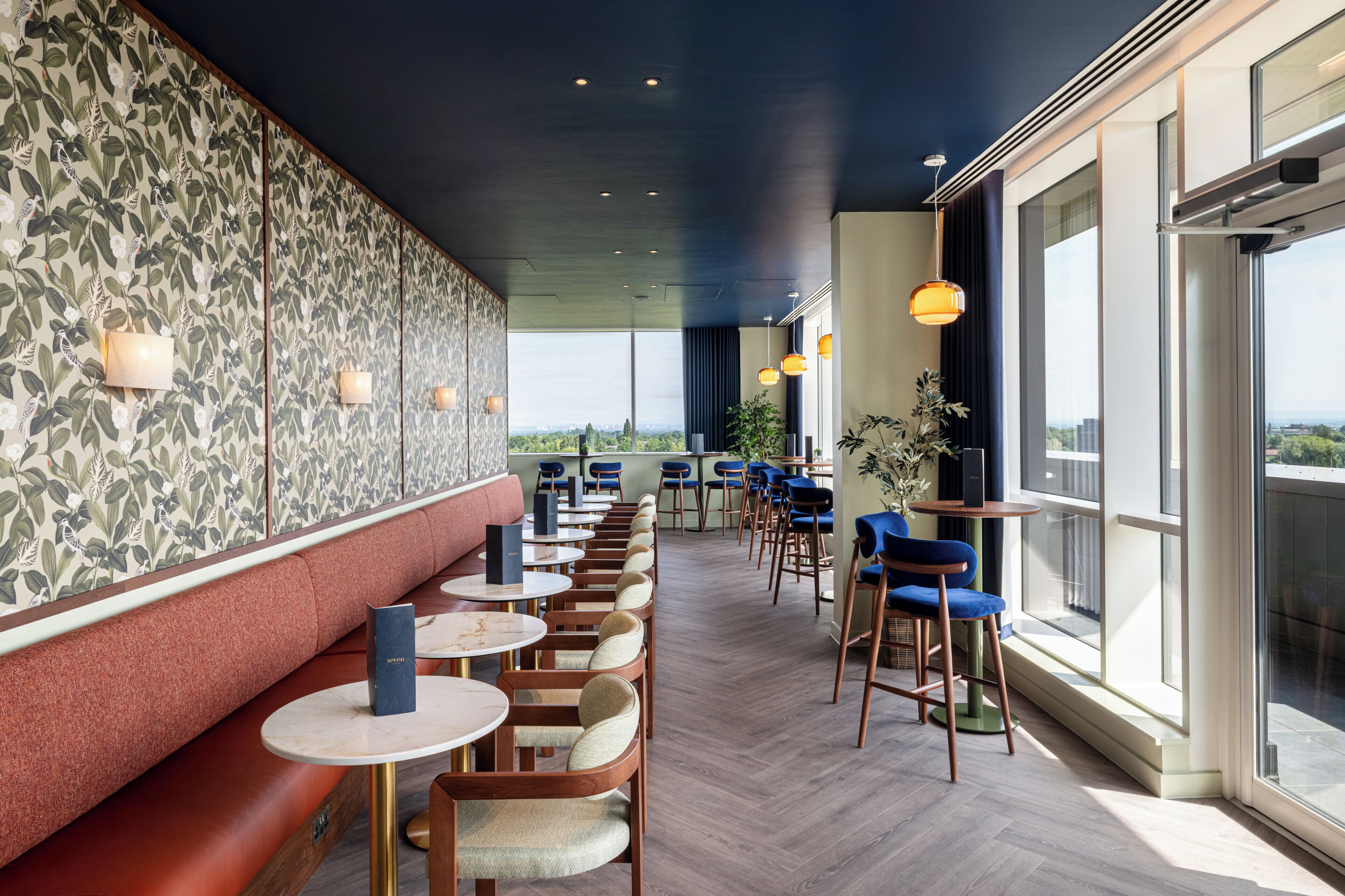 Un restaurant modern amb una barra llarga, seients amb coixins i il·luminació penjant.