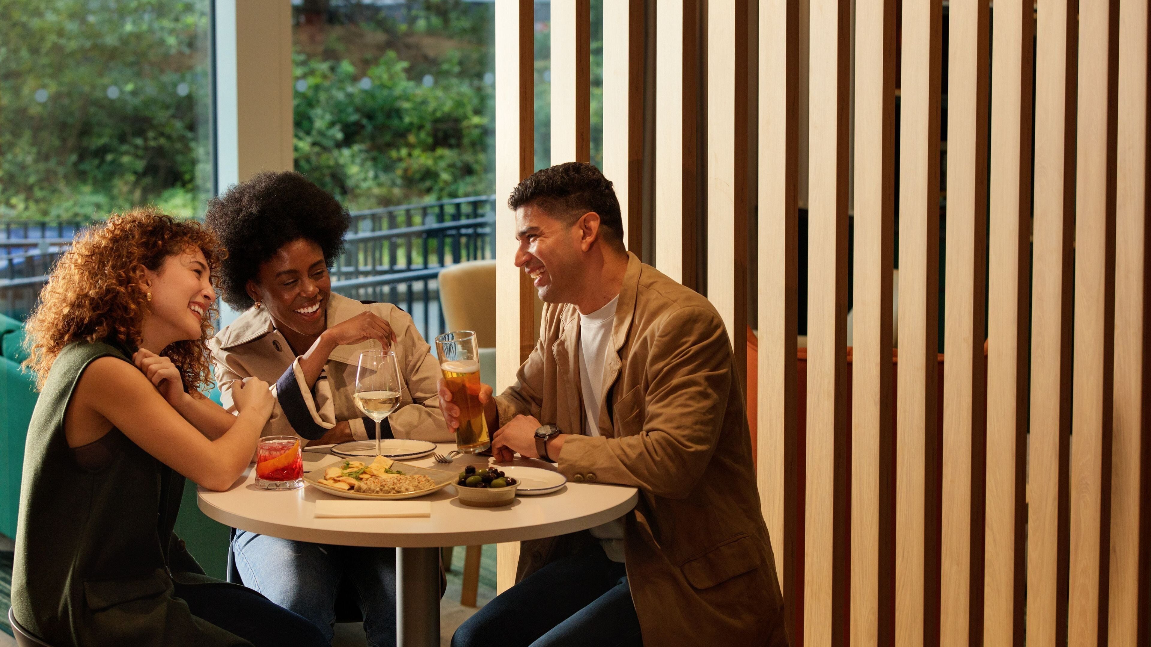 Three people seated at a round table with a meal, glasses, and a beverage.