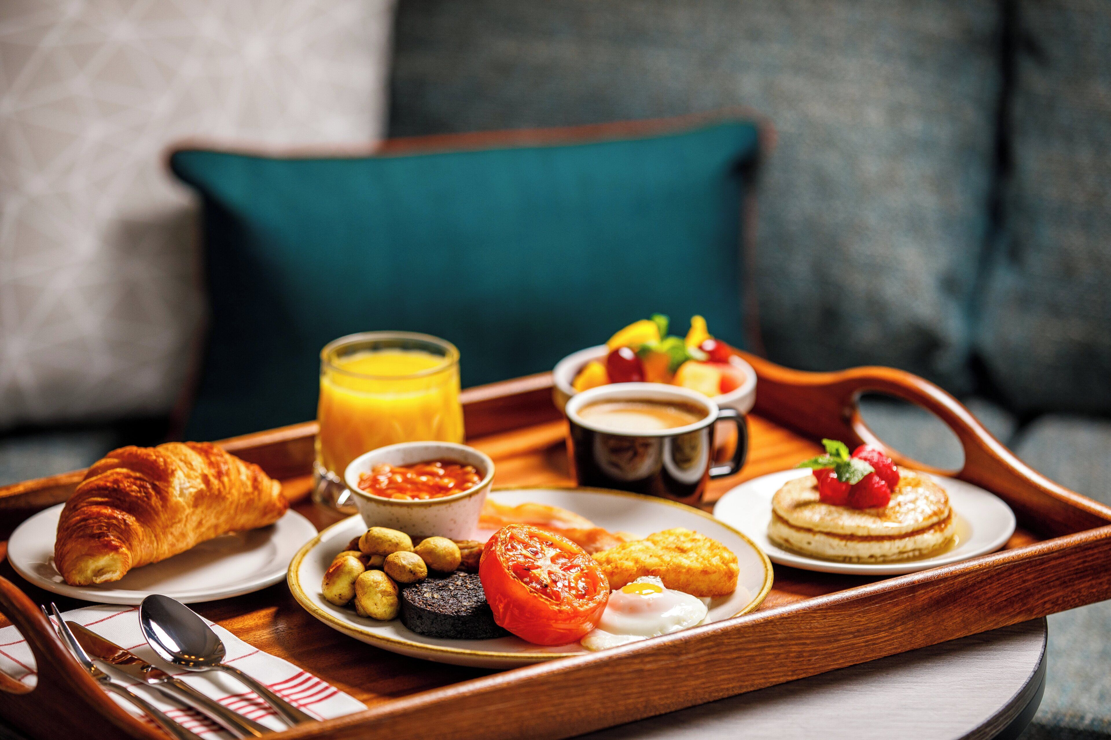 Un plateau de petit-déjeuner avec des croissants, des œufs, des tomates, des olives, des haricots et un verre de jus d’orange.