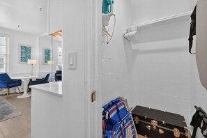 A hotel room with a white door, a small table with chairs, a blue chair, a suitcase, and a coat rack with a jacket. - Offer/PoolStepsToBeach/Dine/Zen Studio (Palm Beach)