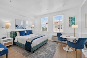 A hotel room with a bed, bedside tables, a desk, chairs, a window, and a painting on the wall. - Offer/PoolStepsToBeach/Dine/Zen Studio (Palm Beach)
