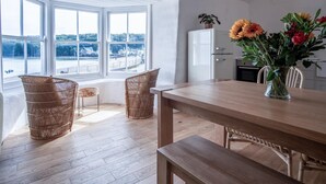 A modern kitchen with a wooden table, wicker chairs, and a view of a waterfront. - Brook Cottage Green - 2 Bedroom Cottage - Dale (Haverfordwest)