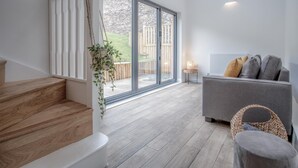 A modern living room with a grey sofa, a wicker chair, and a staircase with wooden steps. - Brook Cottage Green - 2 Bedroom Cottage - Dale (Haverfordwest)