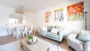 Un salon moderne avec un canapé bleu clair, un canapé blanc, une table basse en bois et un coin repas comprenant des chaises blanches et une table en bois.