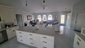 Een ruime keuken met een centraal eiland, witte kastjes en een zithoek met een bank en stoelen.