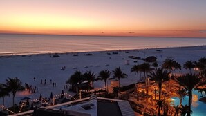 Een resort met een zwembad, strand en uitzicht op de zonsondergang.