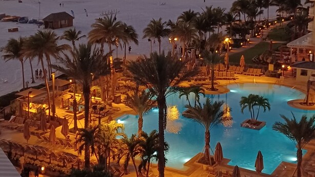 Een resort met een zwembad, palmbomen en uitzicht op het strand.
