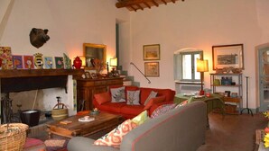 A cozy living room with a fireplace, a red sofa, a wooden coffee table, and various decorative items. - I run away to Umbria, Monti (Umbria)