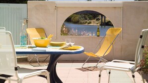 A table with yellow chairs, a bottle, and glasses, with a view of a river and bridge through an archway.