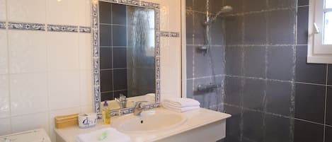 Un baño con un lavamanos blanco, un espejo grande y una zona de ducha con azulejos oscuros.
