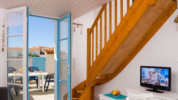A room with a wooden staircase, a television, and a table with chairs.