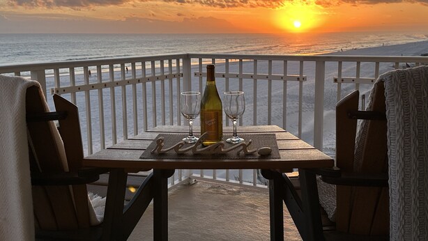 A table with a bottle and glasses on a balcony overlooking the ocean at sunset. - Saltwater+Sunsets: 2 King bdrms/2ba Oceanfront Escape Awaits! (Gulf Shores)