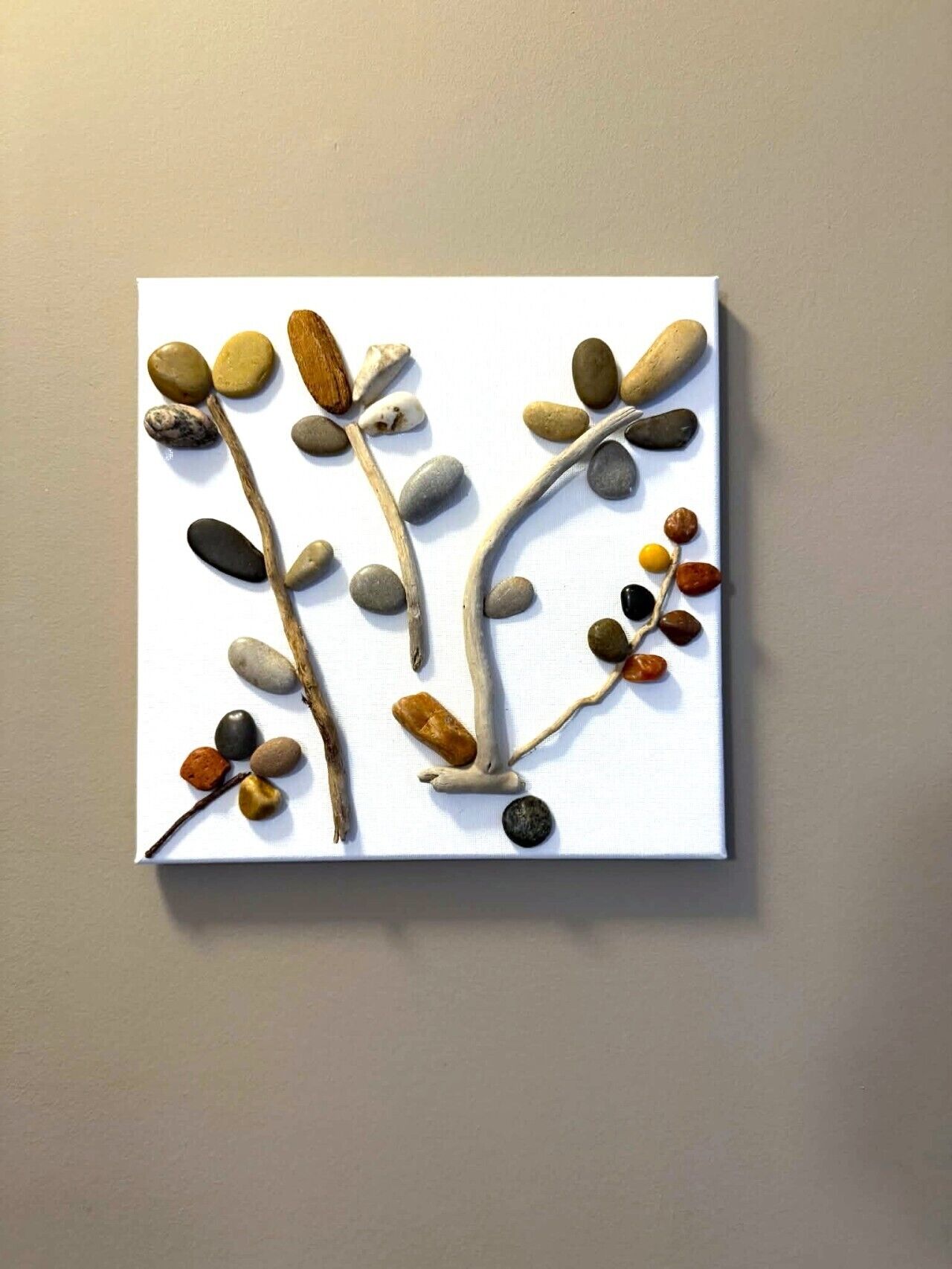 Obra de arte quadrada com ramos e pedras.