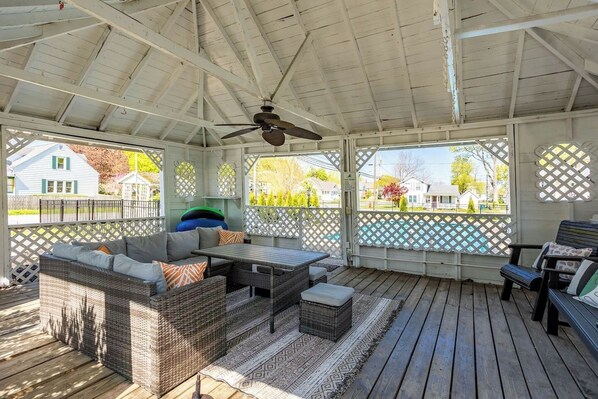 A covered patio with wicker furniture, a ceiling fan, and a view of a residential area. - Old Plat Homestead -pool & walk to beach (Huron)