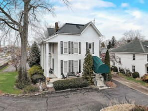 A two-story white house with a front porch, a green umbrella, and a well-maintained lawn. - Old Plat Homestead -pool & walk to beach (Huron)