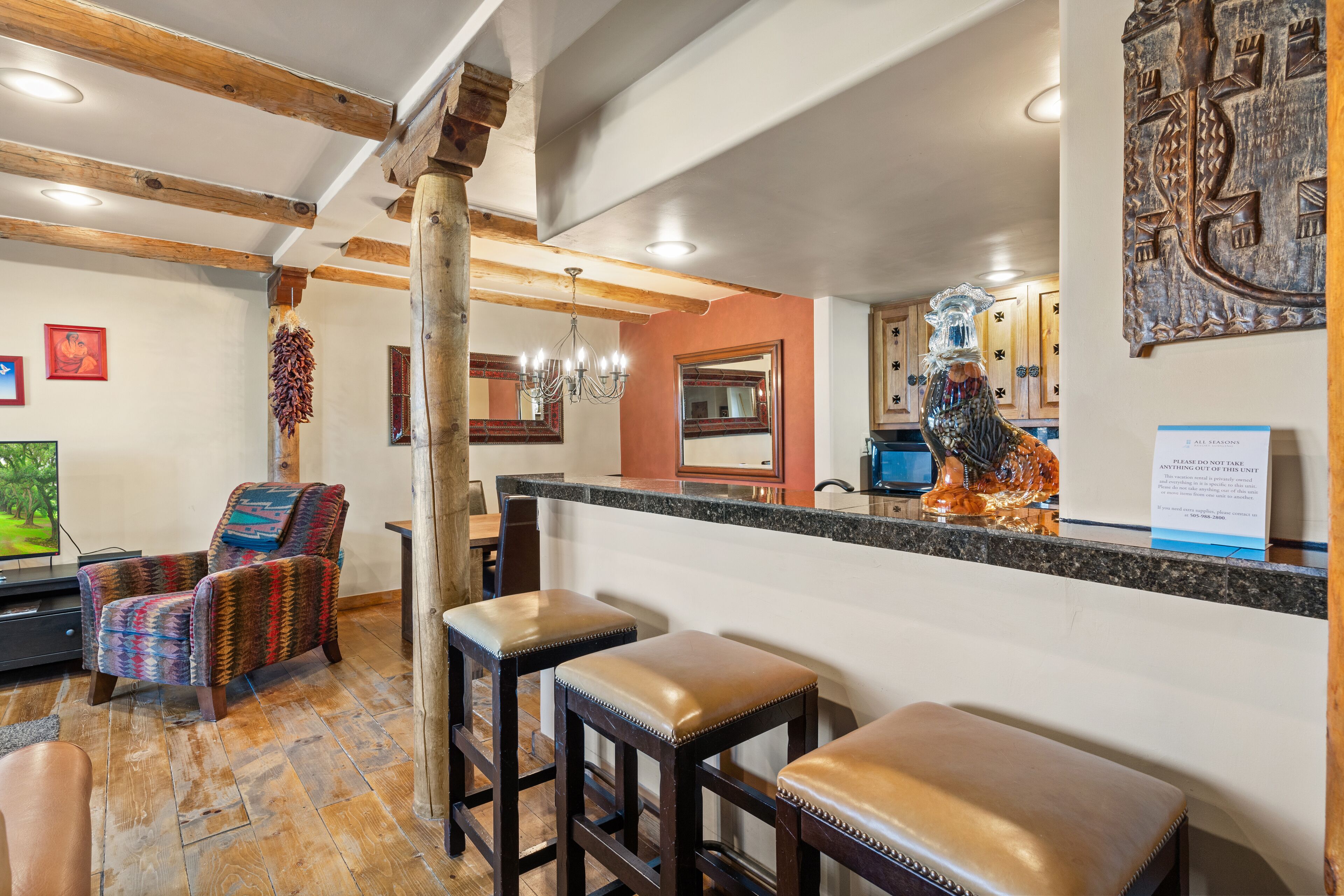Un interior acogedor con techo de madera, una zona de bar con taburetes y una cocina al fondo.