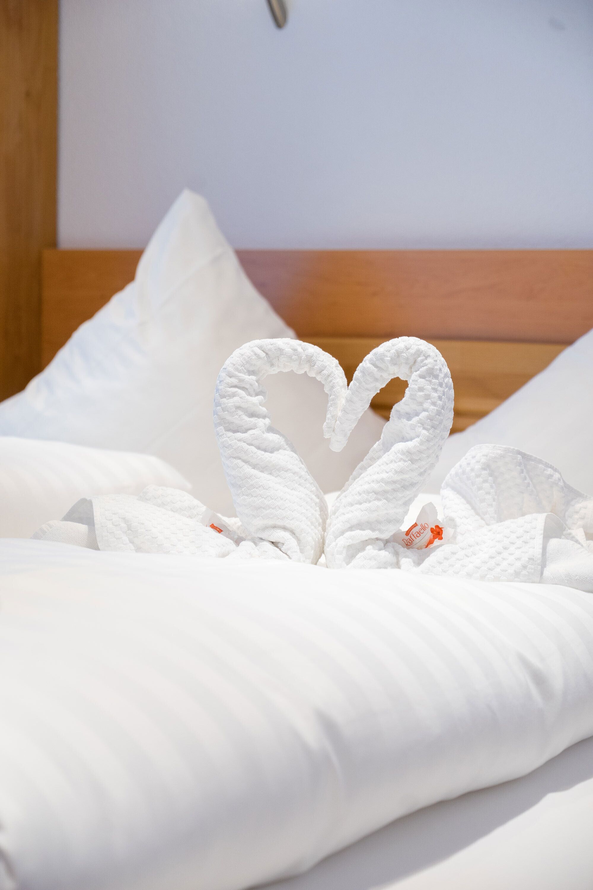 A bed with white bedding and a heart-shaped towel arrangement.