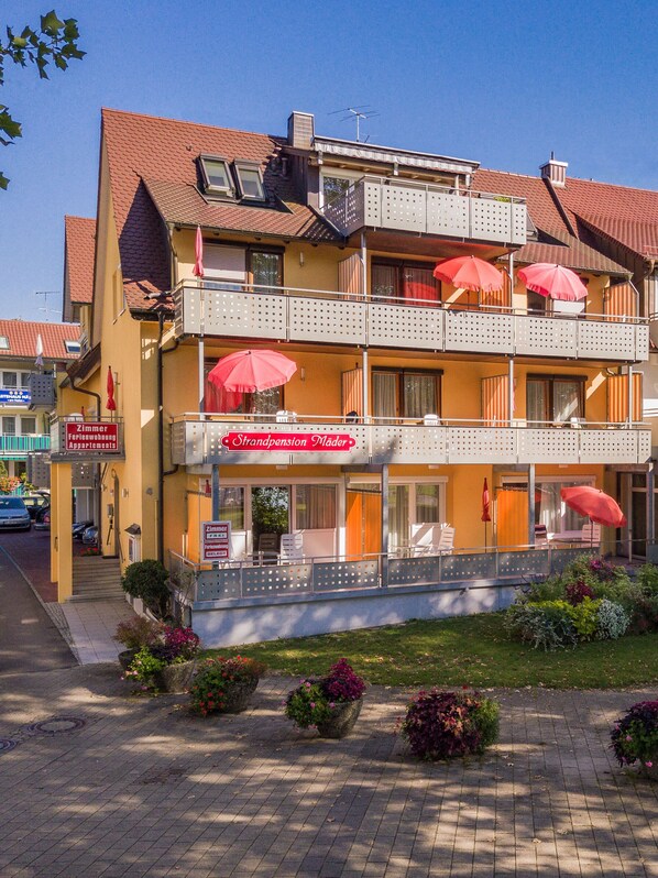 A multi-story hotel with balconies, outdoor seating, and flower arrangements. - Strandpension Mäder (Uhldingen-Muehlhofen)