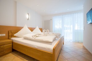 A neatly made bed with white linens and pillows, a wooden headboard, a bedside table with drawers, and a large window with sheer curtains. - Strandpension Mäder (Uhldingen-Muehlhofen)