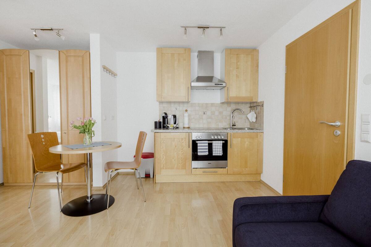 A compact kitchen with wooden cabinets, a built-in oven, and a dining area with a round table and two chairs.