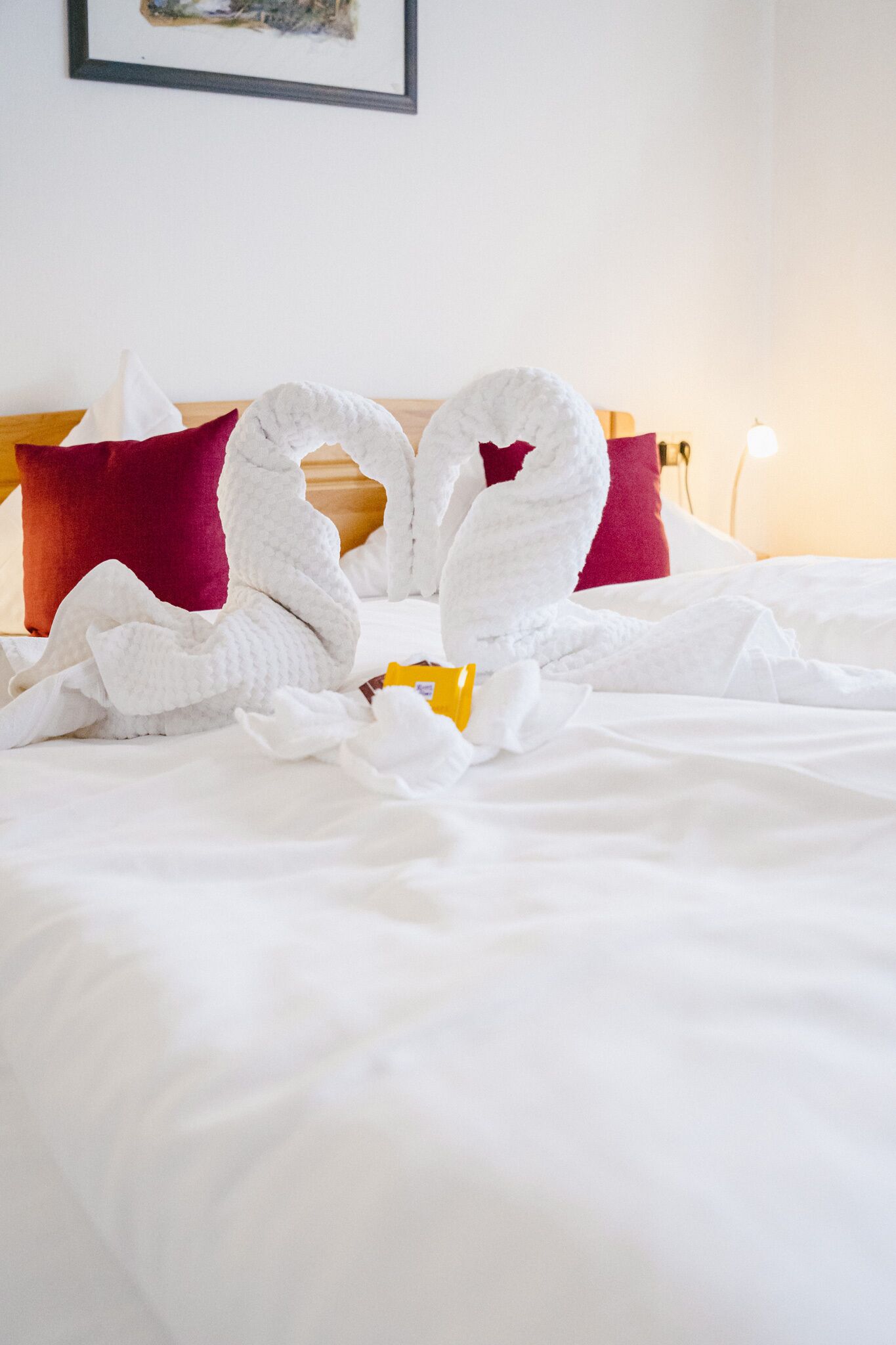 Ein Hotelzimmer mit einem ordentlich bezogenem Bett, zwei zu Schwänen geformten Handtüchern und einem gelben Gegenstand auf dem Bett.