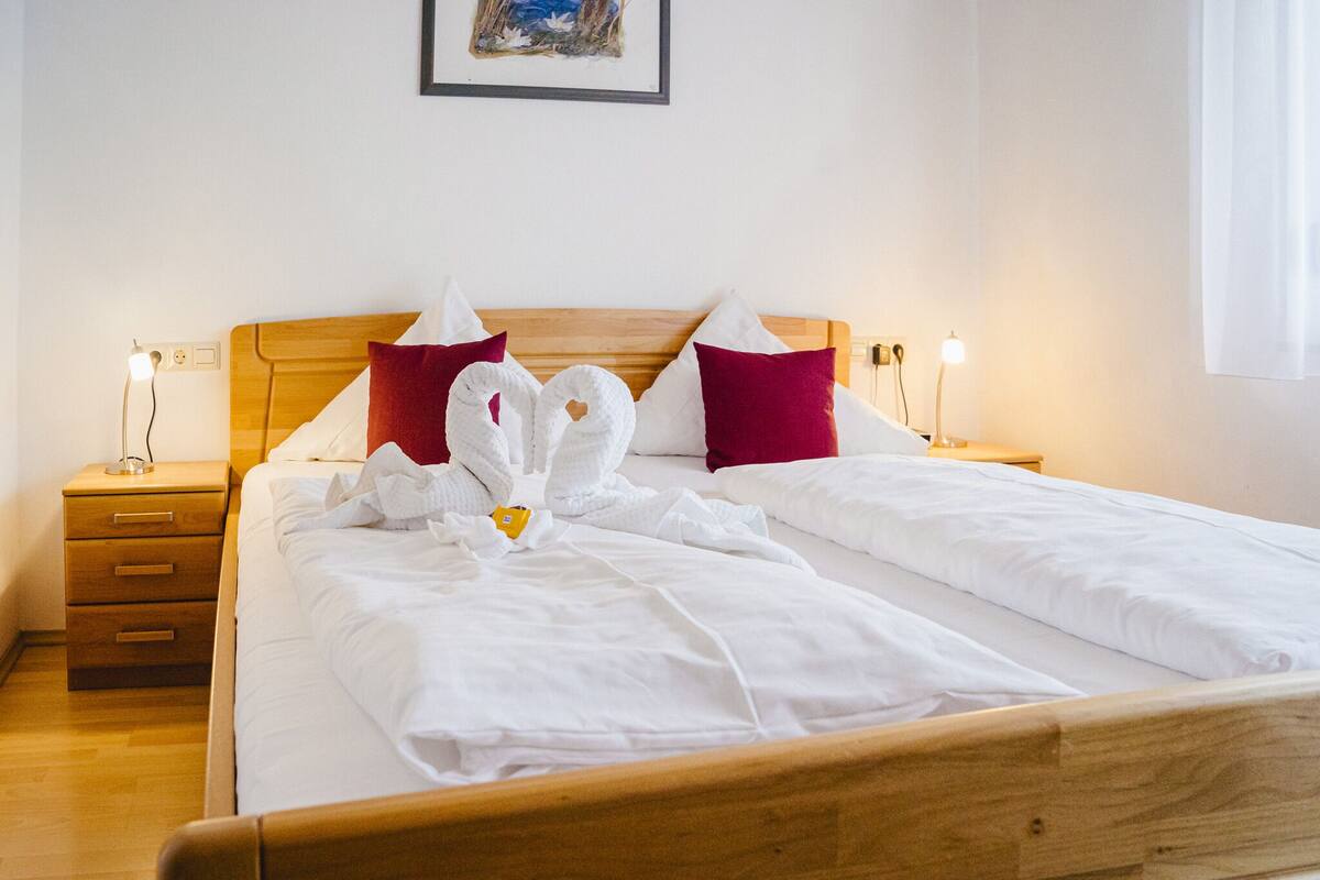 A neatly made bed with white linens and red pillows, a wooden headboard, and bedside tables with lamps.