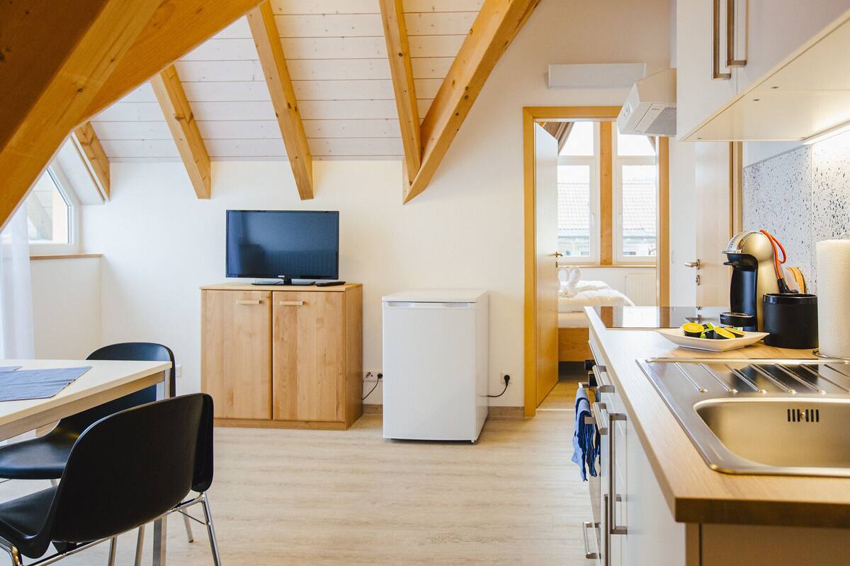 A compact kitchen with wooden beams, a refrigerator, a sink, and a television.