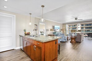 A spacious living area with a large wooden island, a dining table, and a view of a multi-story building. - Honua Kai | Ocean View 2 BR | Wrap Around Lanai | Car Incl. w/ 6+ Nights | HKK-309 by KBM (Lahaina)