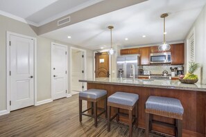 Cucina con isola centrale, mobili in legno, elettrodomestici in acciaio inossidabile e lampadario a sospensione.
